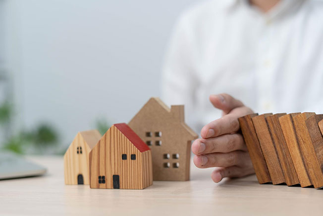 A man’s hand stops wood blocks from falling on a wooden model house